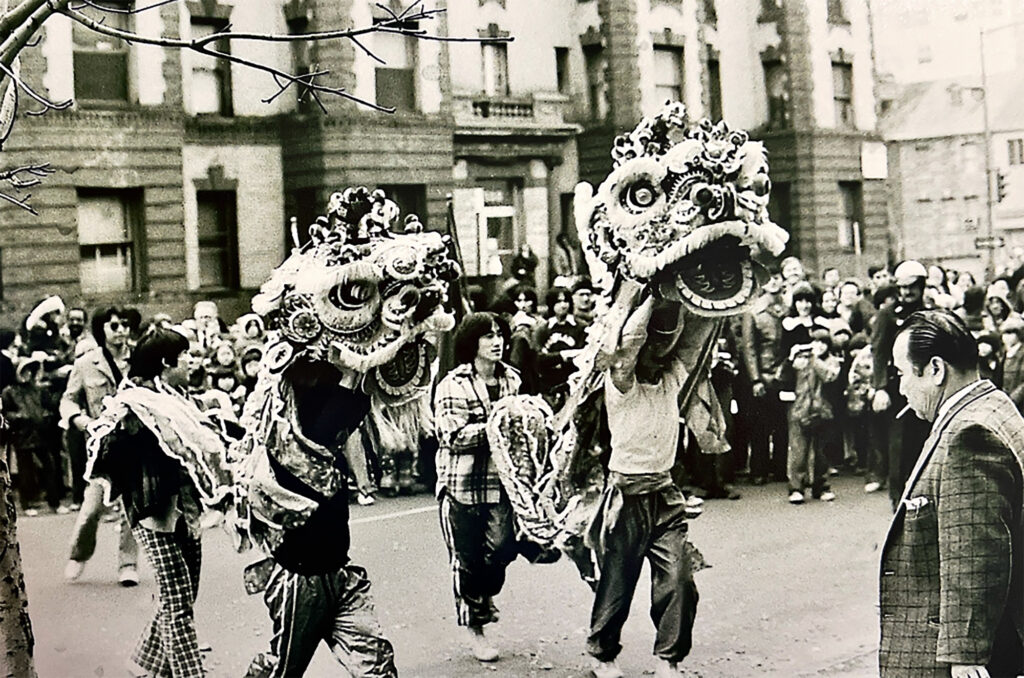 A black and white photo of Lion Dancers in front of an audience in Washington, D.C.'s Chinatown.