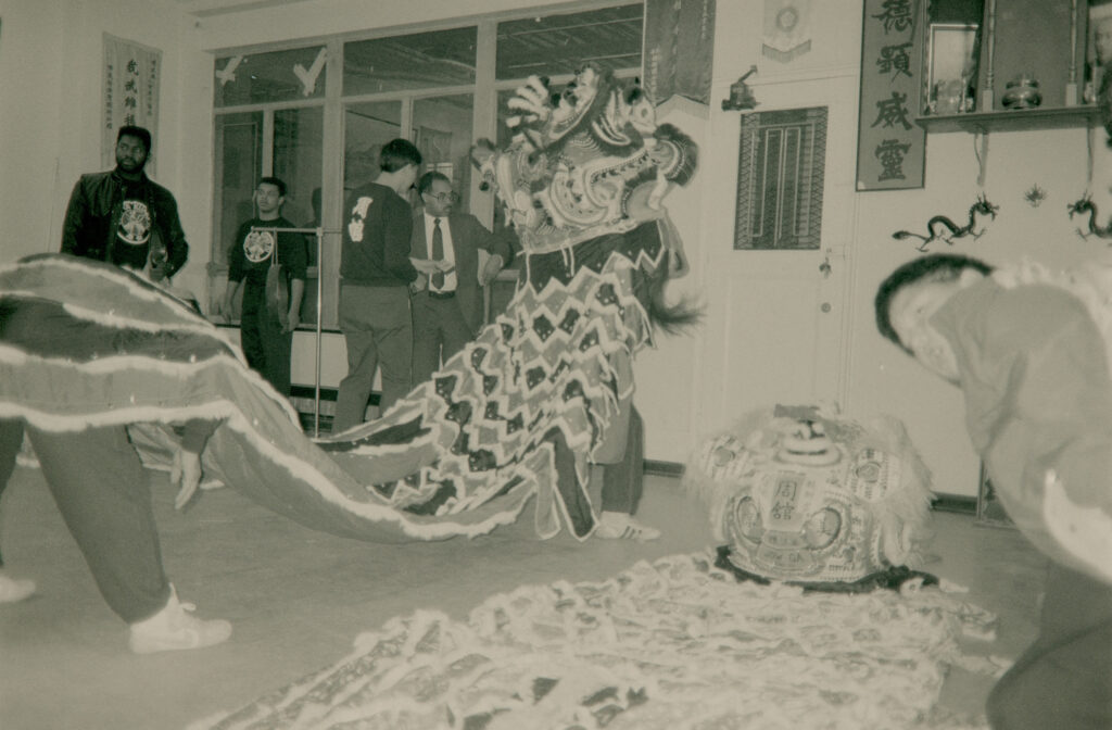 A performer holding a Lion Dance costume prepares with others in a room.