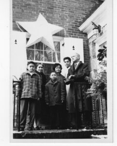 A family stands together on the front steps of their home underneath a large Filipino star-shaped parol.