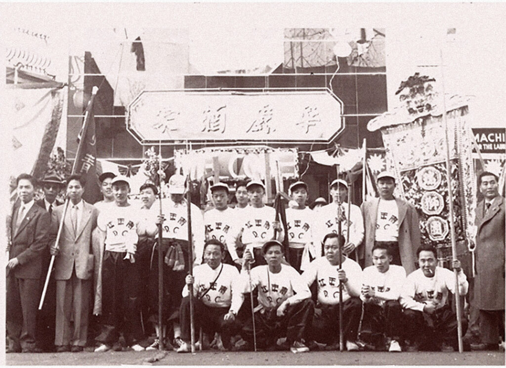 A black and white photo of a group of people holding bamboo sticks and posing.