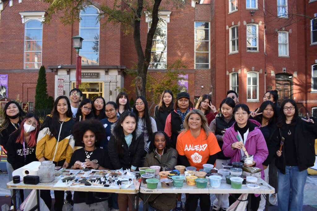 A large group of youth stand with tables holding paint and brushes in front of the Chinese Community Church.