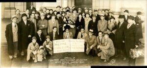 A large group of people wearing suits and coats pose in Union Station with signs welcoming the Philippine Independence Delegation.