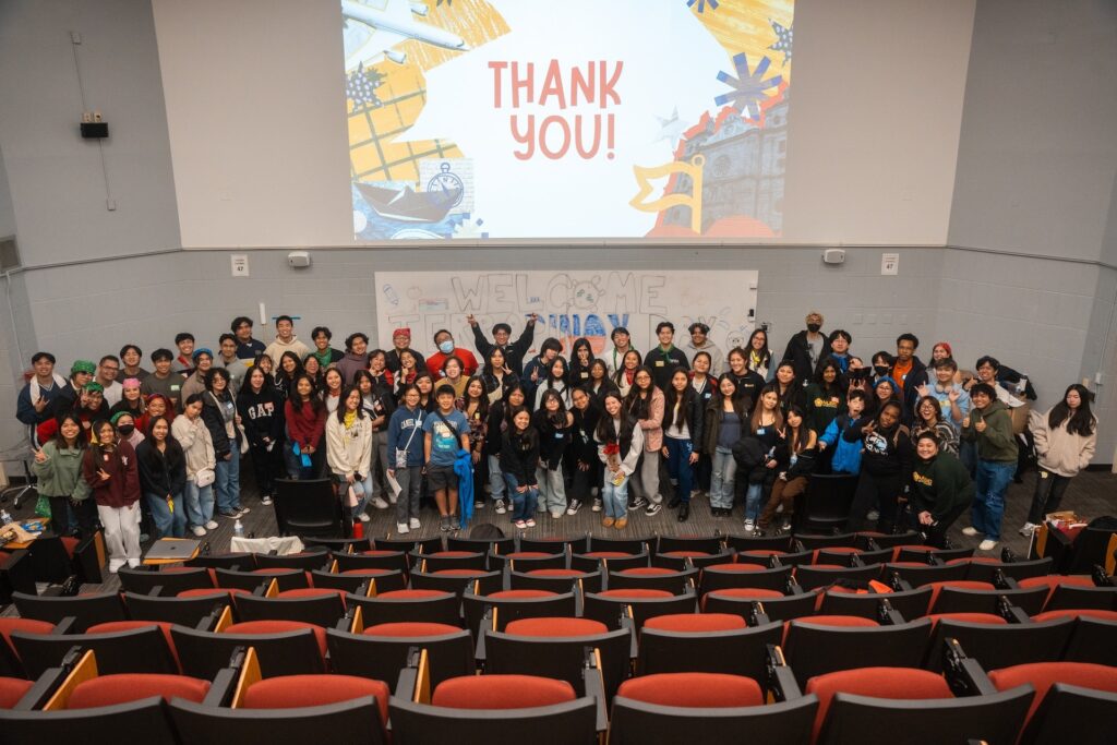 A group of youth pose for a photo in front of a university lecture hall in front of a projection that says "THANK YOU!"