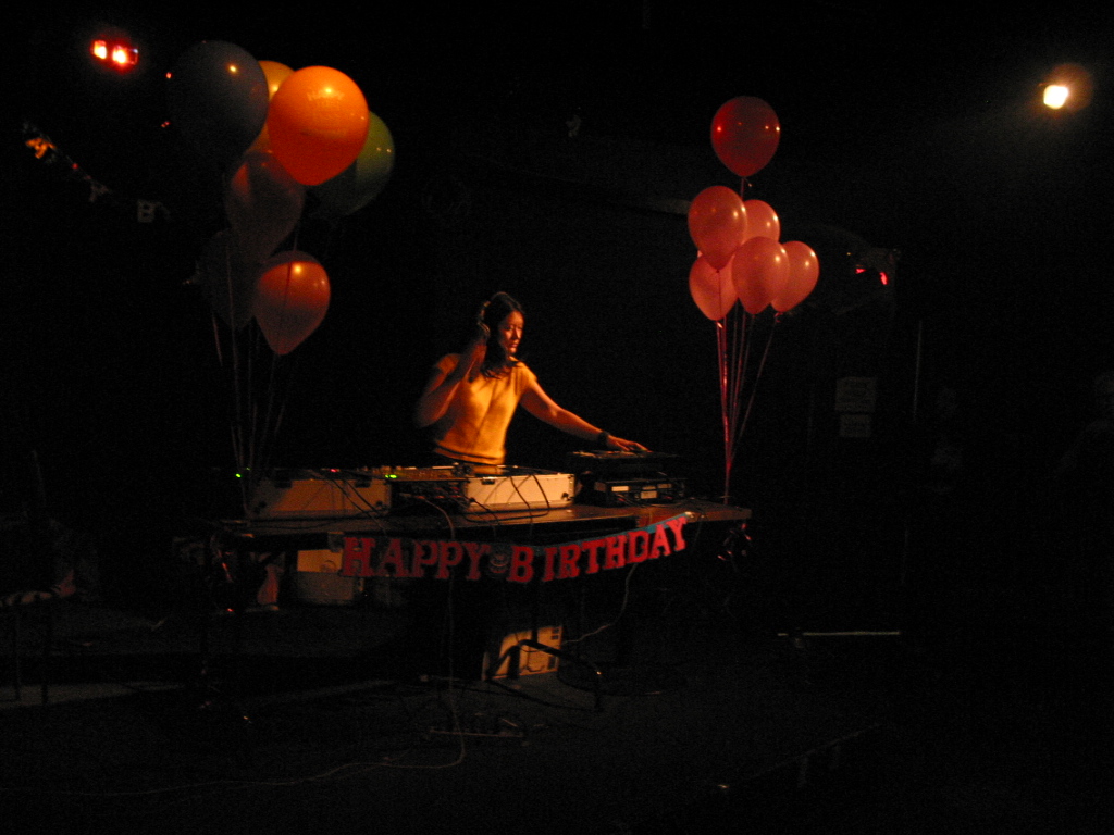 A DJ with turntables, surrounded by balloons and with letters strung in front of the table reading "Happy Birthday."