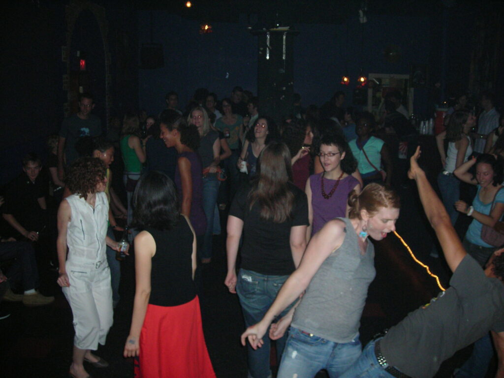 A large group of people, mostly women, dancing in a dark room.