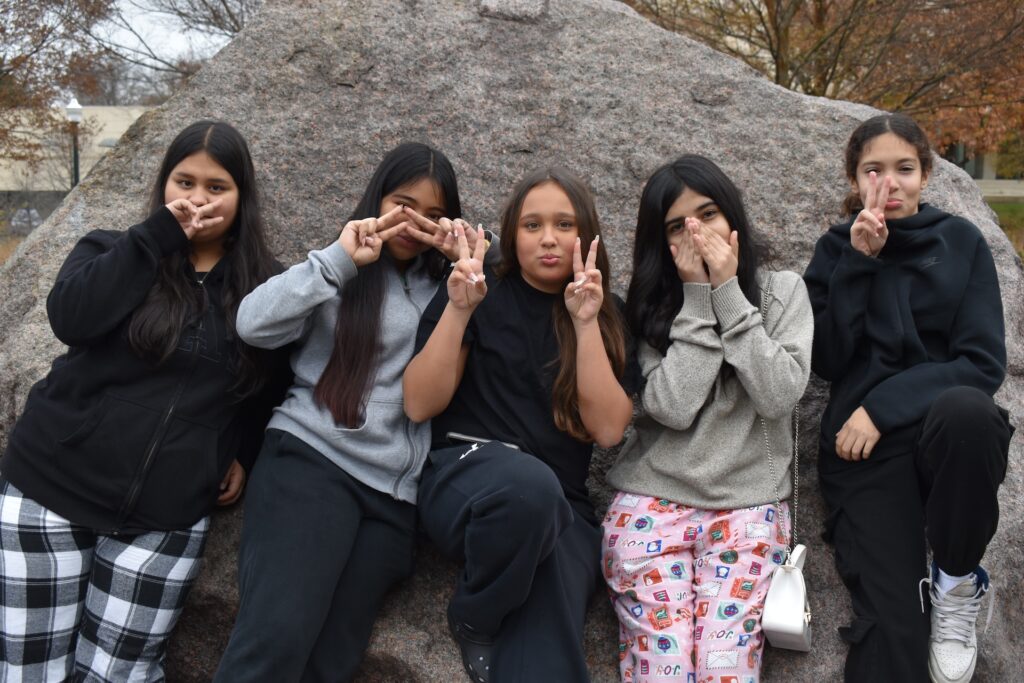 Five young people pose for a photo while standing in front of a large gray boulder.