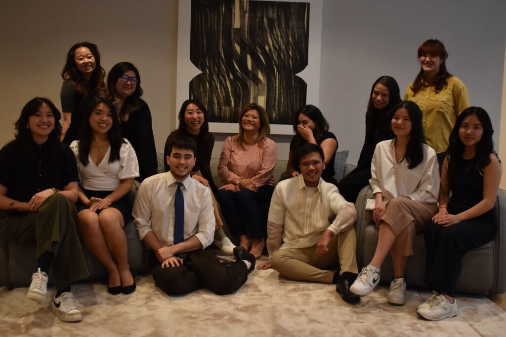 A group of youth and two adults pose for a photo while sitting on a sofa in front of a black and white artwork.