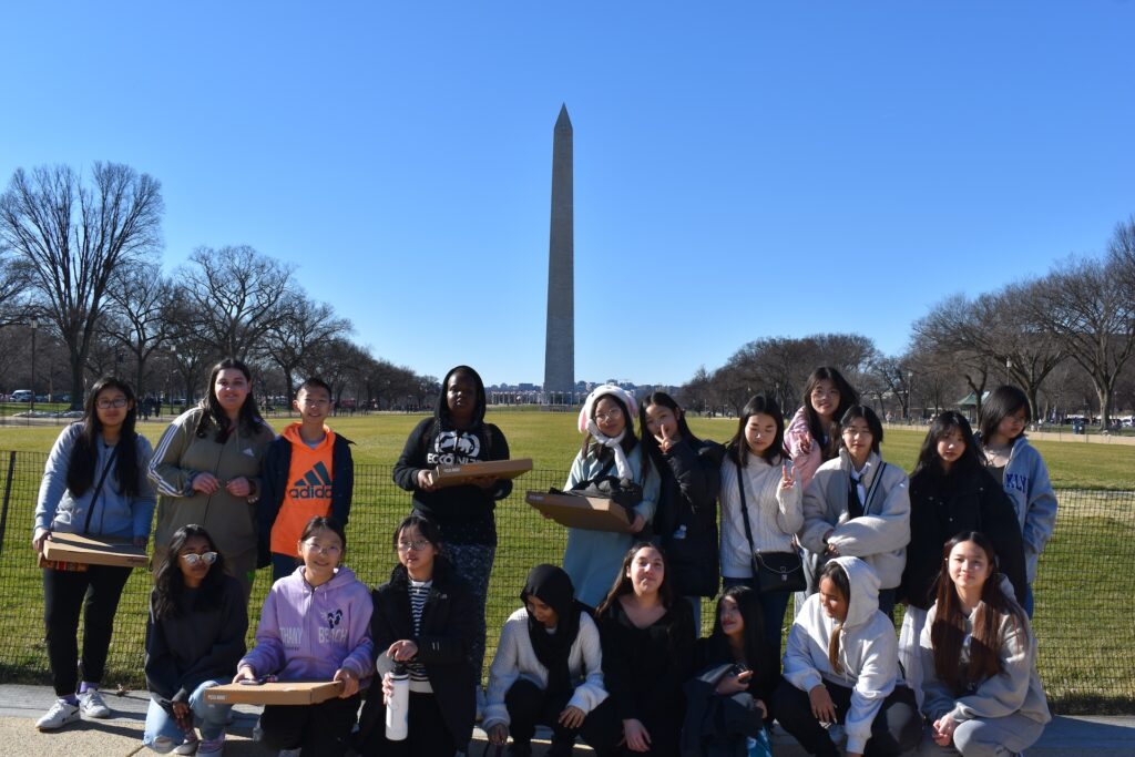 A group of youth pose for a photo while standing in the National Mall in front of the Washington Monument.