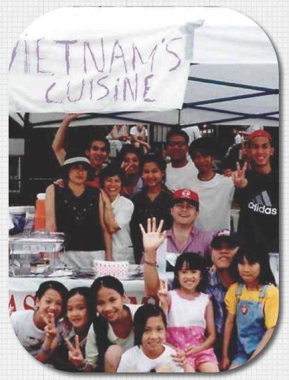 A group of people pose together for a photo in a food stall with a sign that reads "Vietnam's Cuisine."