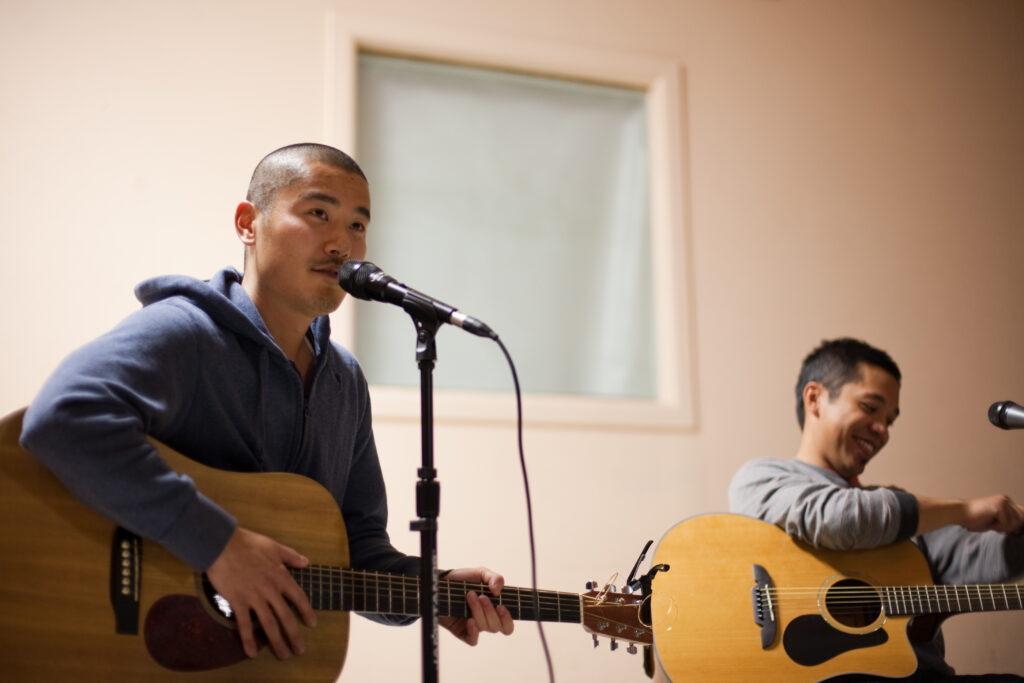 Two performers with guitars speaking into microphones.