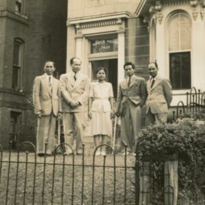 Five people pose for a photo on the lawn of a rowhouse.